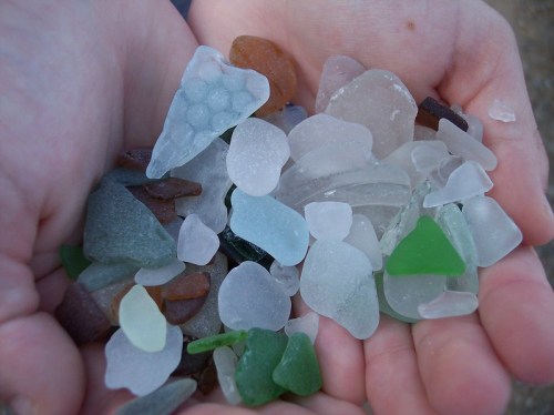 A pair of hands holding a colorful assortment of smooth sea glass pieces in various shapes and colors.