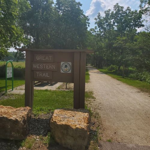 Sign for the Great Western Trail, surrounded by trees and a gravel path leading into the distance.