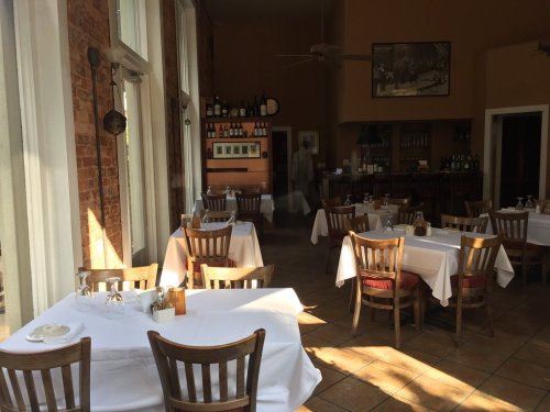 A cozy restaurant interior with wooden tables, white tablecloths, and a bar area in the background.