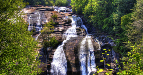 A cascading waterfall flows down rocky cliffs, surrounded by lush green trees and foliage.