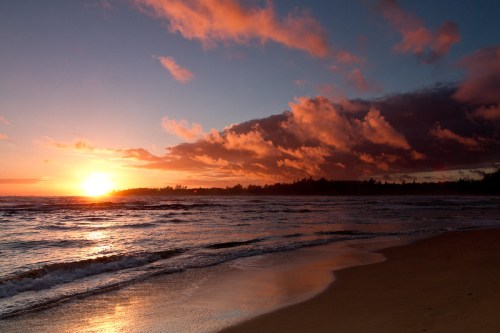 A serene beach at sunset, with vibrant clouds reflecting on the water and gentle waves lapping at the shore.