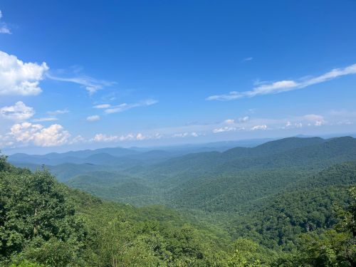 A panoramic view of lush green mountains under a bright blue sky with scattered clouds.