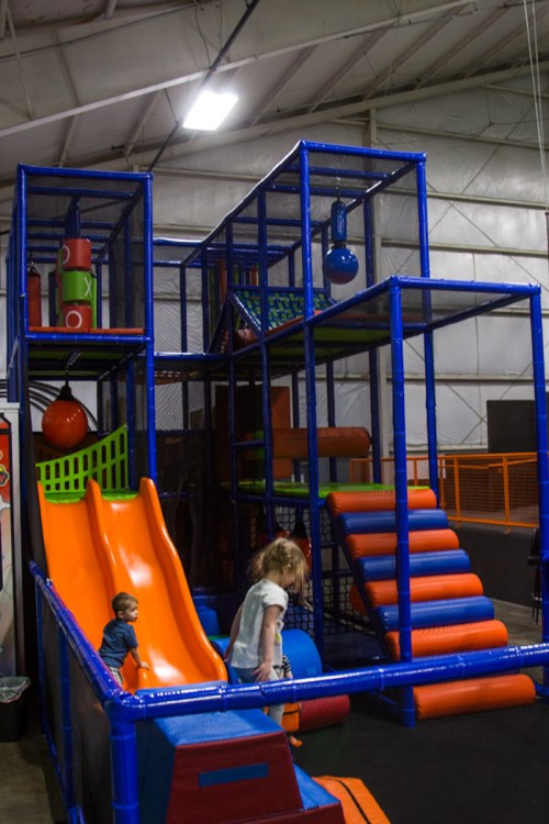 Colorful indoor playground with slides, climbing structures, and children playing.