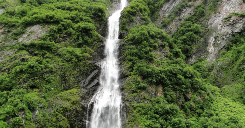 A cascading waterfall flows down a lush, green mountainside surrounded by dense vegetation.
