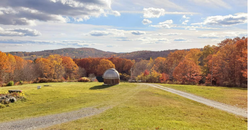 A scenic view of rolling hills and colorful autumn trees, featuring a small dome structure on a grassy field.