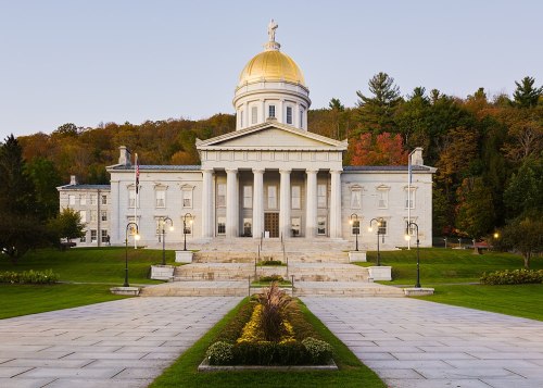 A grand building with a golden dome, surrounded by greenery and autumn trees, featuring steps and decorative lights.