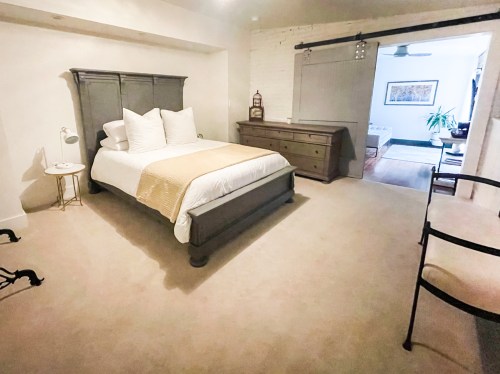 A cozy bedroom featuring a gray bed frame, white bedding, a wooden dresser, and soft lighting.