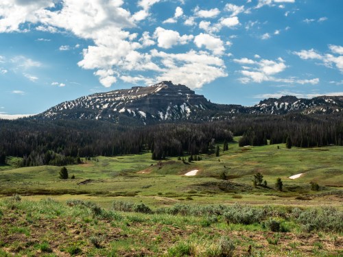 A scenic view of a mountain range with green meadows and scattered clouds in a blue sky.