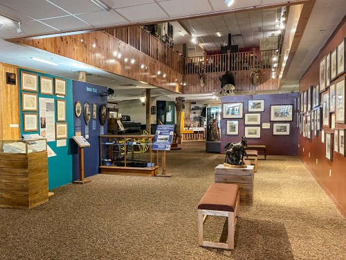 A spacious museum interior with framed artwork, informational displays, and wooden benches in a warmly lit setting.