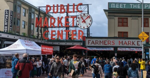 Crowd at the Public Market Center, with a sign for the Farmers Market and a festive atmosphere.