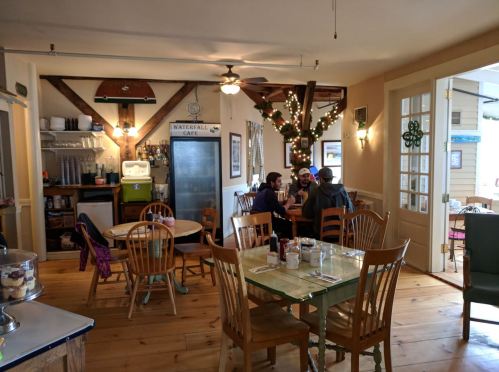 Cozy café interior with wooden beams, tables, and patrons enjoying a meal, decorated with lights and greenery.