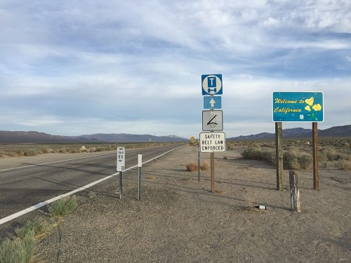 A highway sign indicating the welcome to California, with safety belt law and other road signs in a desert landscape.