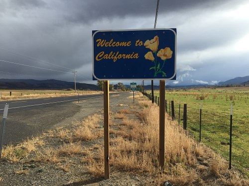 A "Welcome to California" sign with poppy flowers, set against a cloudy sky and open road.