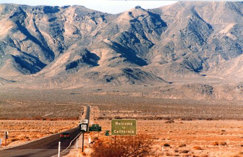 A scenic view of a highway leading to mountains, with a "Welcome to California" sign in the foreground.
