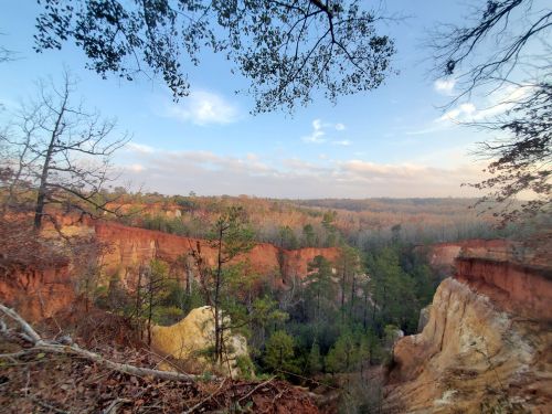 A scenic view of a canyon with colorful rock formations and trees, under a clear sky with soft clouds.