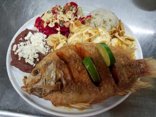 A plate of fried fish garnished with lime, served with rice, beans, salad, and tortilla chips.