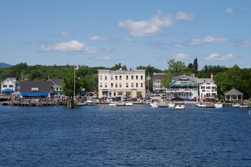 A scenic waterfront view featuring boats, shops, and trees under a clear blue sky.