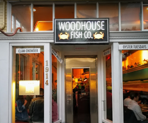 Exterior of Woodhouse Fish Co. restaurant, featuring a sign and large windows, with diners visible inside.