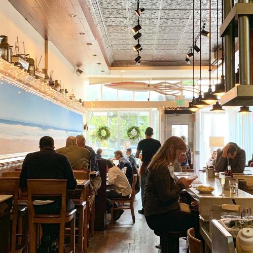 A cozy restaurant interior with wooden seating, beach-themed decor, and patrons enjoying their meals and conversations.