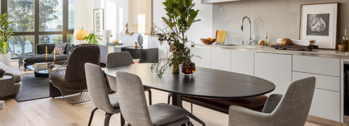 A modern dining area with a round table, stylish chairs, and a view of greenery through large windows.