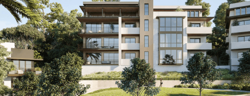 Modern multi-story building surrounded by greenery, featuring large windows and balconies, set in a landscaped area.
