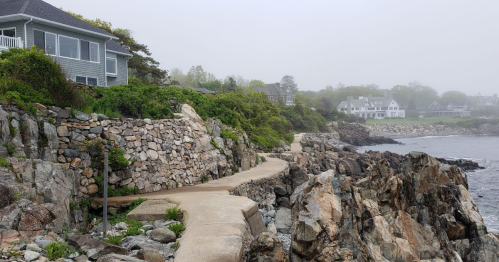 A foggy coastal scene featuring a rocky shoreline, a winding path, and houses nestled among greenery.