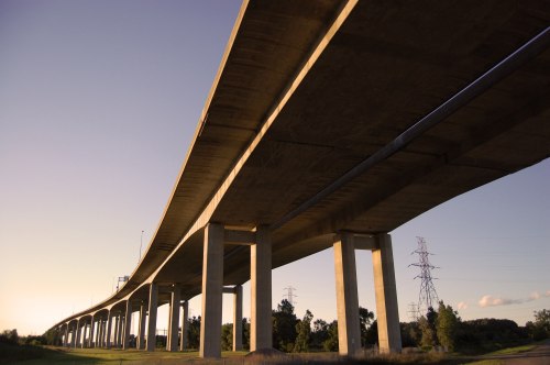 A concrete overpass supported by tall pillars, with a clear sky and power lines in the background.
