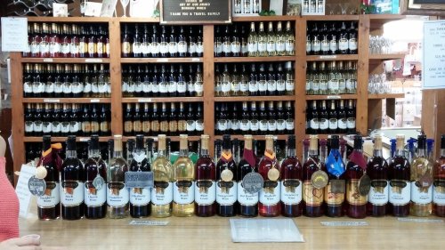 A wooden counter displaying various bottles of wine and spirits, with shelves of more bottles in the background.