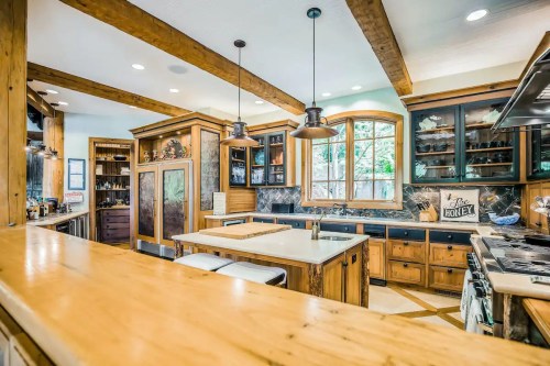 A spacious kitchen with wooden beams, dark cabinetry, and a large island, featuring modern appliances and natural light.