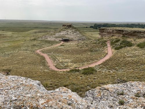 A winding path leads through grassy hills and rocky formations in a vast, open landscape.