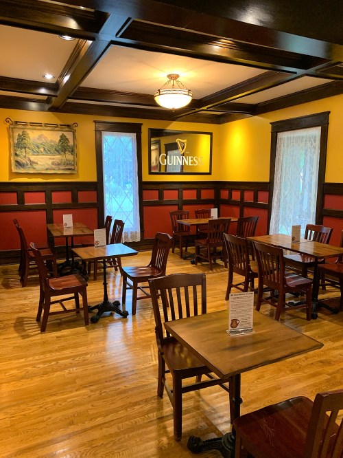 Cozy restaurant interior with wooden tables and chairs, yellow and red walls, and a Guinness sign on the wall.