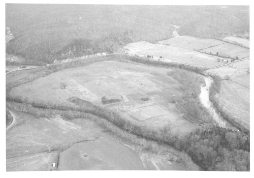 Aerial view of a rural landscape with fields, a river, and wooded areas, captured in black and white.