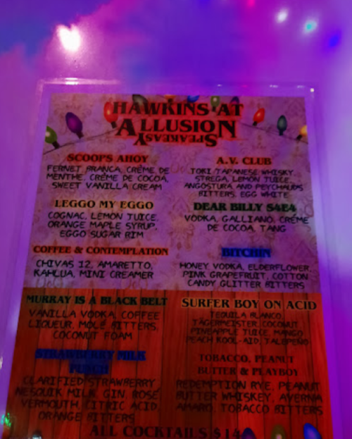 A colorful cocktail menu featuring creative drink names and ingredients, illuminated by vibrant lights.