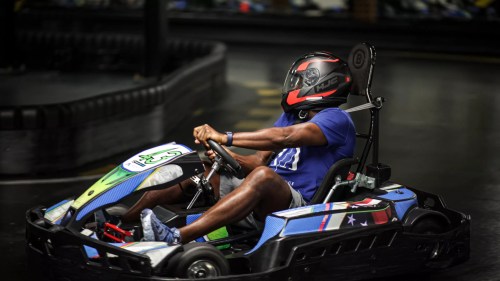 A person in a go-kart wearing a helmet, racing on an indoor track.