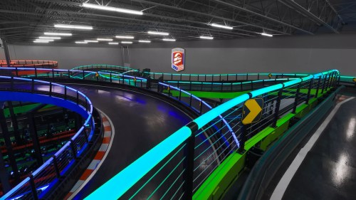 A brightly lit indoor go-kart track with colorful neon lights and a curved design.