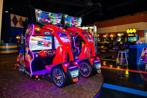 Two vibrant racing arcade games with colorful screens and neon lights, set in a lively gaming arcade.