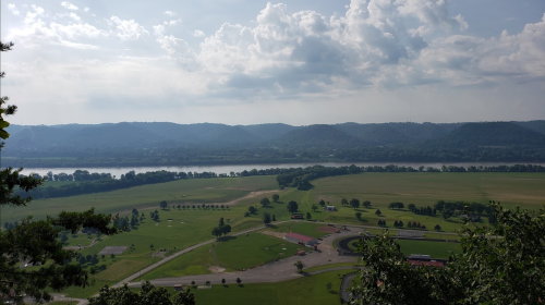 A scenic view of rolling hills, a river, and fields under a partly cloudy sky.