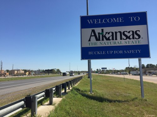 Welcome sign for Arkansas, featuring the text "The Natural State" and "Buckle Up for Safety," alongside a highway.