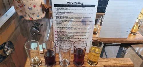 A wooden tasting board with five wine samples and a menu for a wine tasting event.