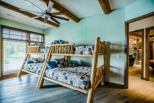 Cozy bedroom featuring rustic bunk beds with colorful bedding and a ceiling fan, set against a light green wall.