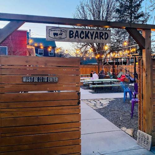 A cozy backyard with string lights, seating areas, and a sign stating "Must be 21 to enter." Trees in the background.