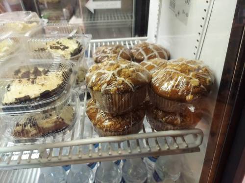 A display case with wrapped muffins and desserts, including chocolate treats and frosted pastries.