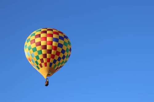 A colorful hot air balloon with a checkered pattern floats against a clear blue sky.