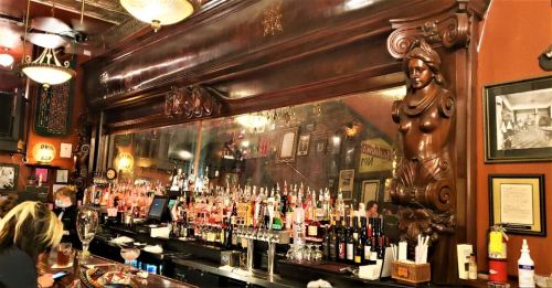 A vintage bar with ornate wooden decor, a mirrored back, and shelves lined with various bottles of alcohol.