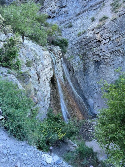 A waterfall cascading down a rocky cliff surrounded by greenery in a mountainous landscape.