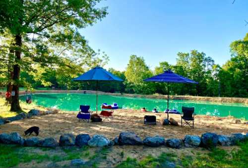 A serene lakeside scene with two blue umbrellas, chairs, and a rocky border, surrounded by lush greenery.