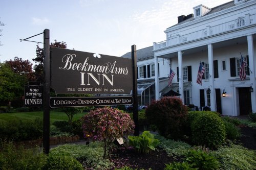 Sign for Beekman Arms Inn, the oldest inn in America, with a historic building and lush landscaping.