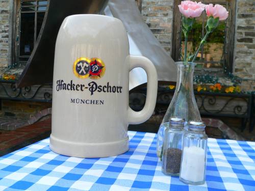 A large beer stein with "Hacker-Pschorr München" on a checkered tablecloth, alongside salt and pepper shakers and flowers.