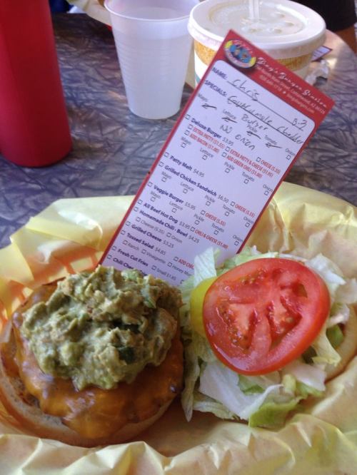 A burger topped with guacamole, cheese, and a side of lettuce and tomato, with an order receipt beside it.