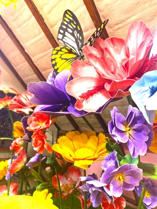 A vibrant arrangement of colorful artificial flowers with a butterfly perched among them.